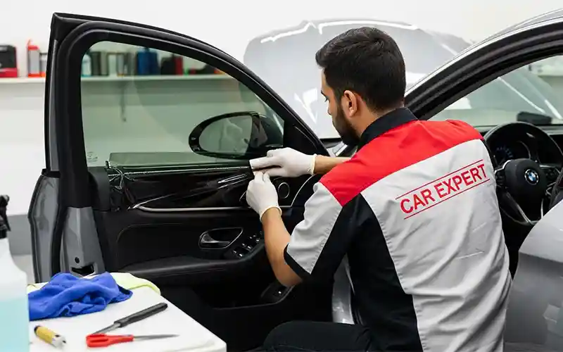 Auto detailing technician applying UV protection films on car windows in Dubai